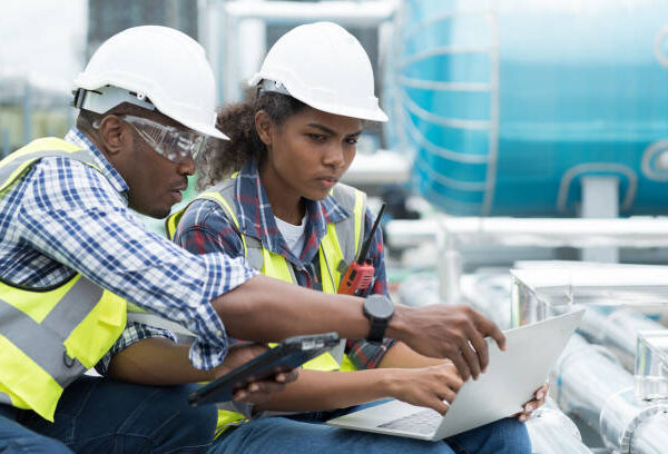 Group of African American engineer working in sewer pipes area at construction site. Male engineer and woman engineer discussing for maintenance sewer pipes, water tank on rooftop of building